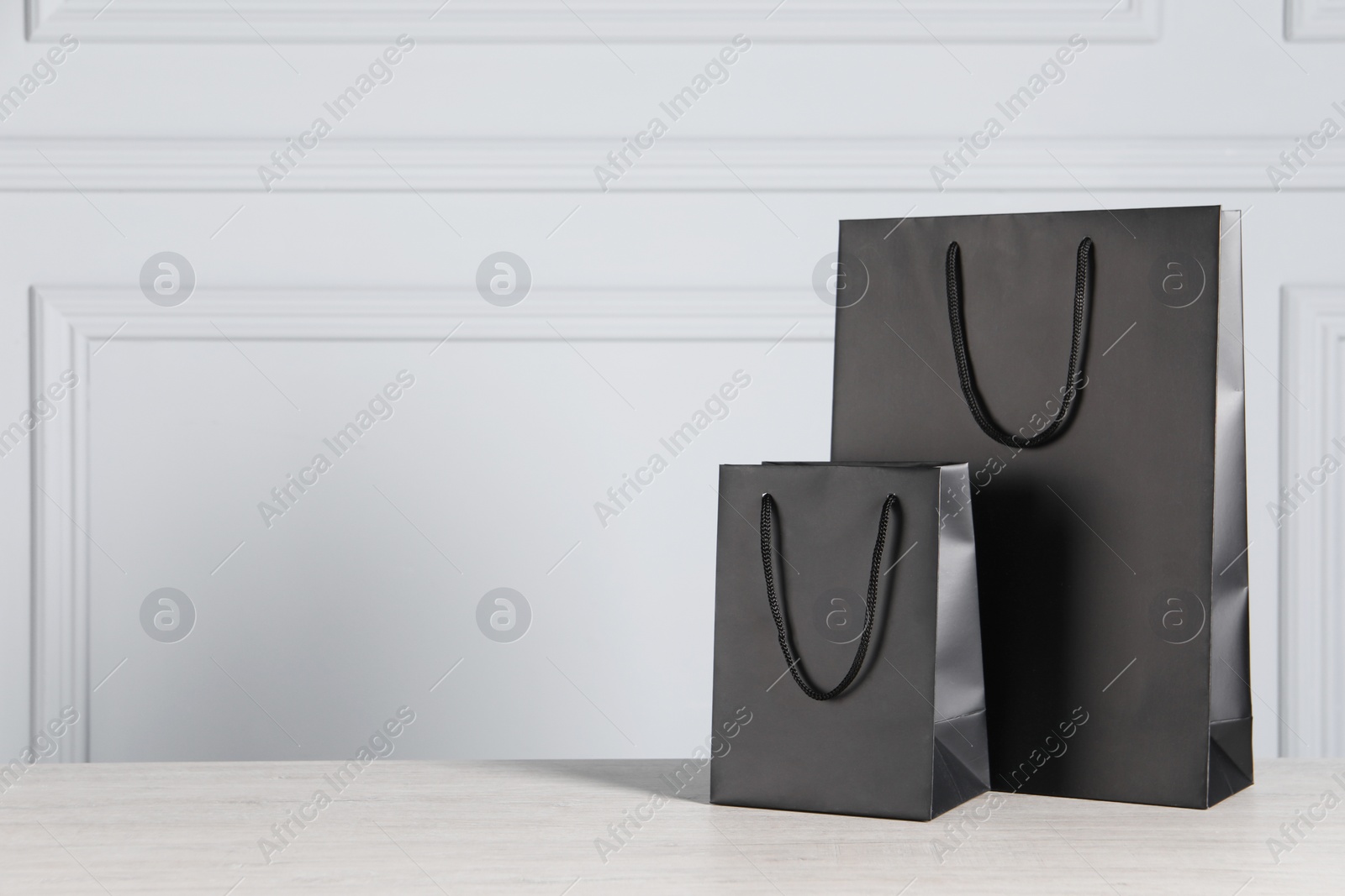 Photo of Black paper bags on wooden table against light grey wall, space for text