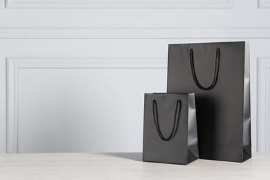 Black paper bags on wooden table against light grey wall, space for text