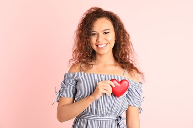 African-American woman holding wooden heart on color background