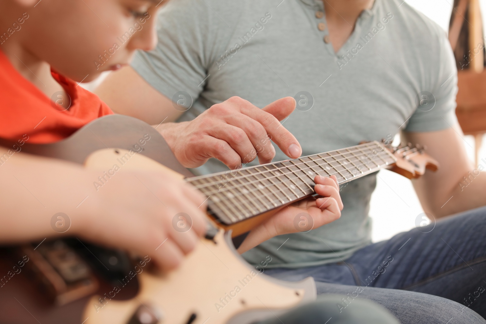 Photo of Little boy playing guitar with his teacher at music lesson, closeup. Learning notes