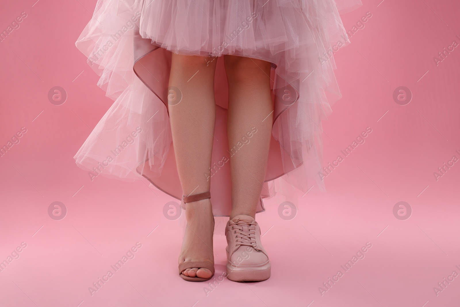 Photo of Woman wearing high heeled shoe and sneaker on pink background, closeup. Glamour vs comfort concept