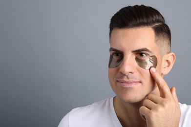 Photo of Man applying dark under eye patch on grey background. Space for text