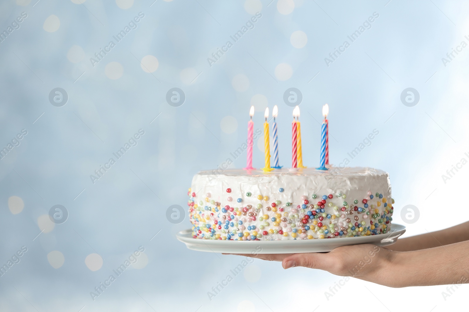 Photo of Woman holding birthday cake with burning candles against blurred background, closeup. Space for text