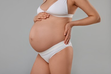 Pregnant woman in stylish comfortable underwear on grey background, closeup