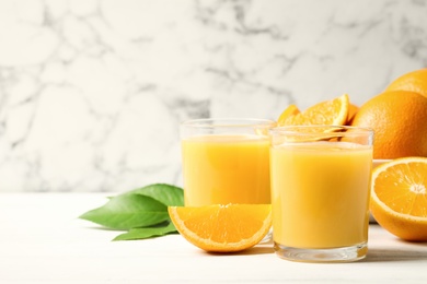 Photo of Glasses of orange juice and fresh fruits on white table. Space for text