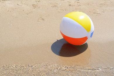 Photo of Colorful beach ball on wet sand at seaside, space for text