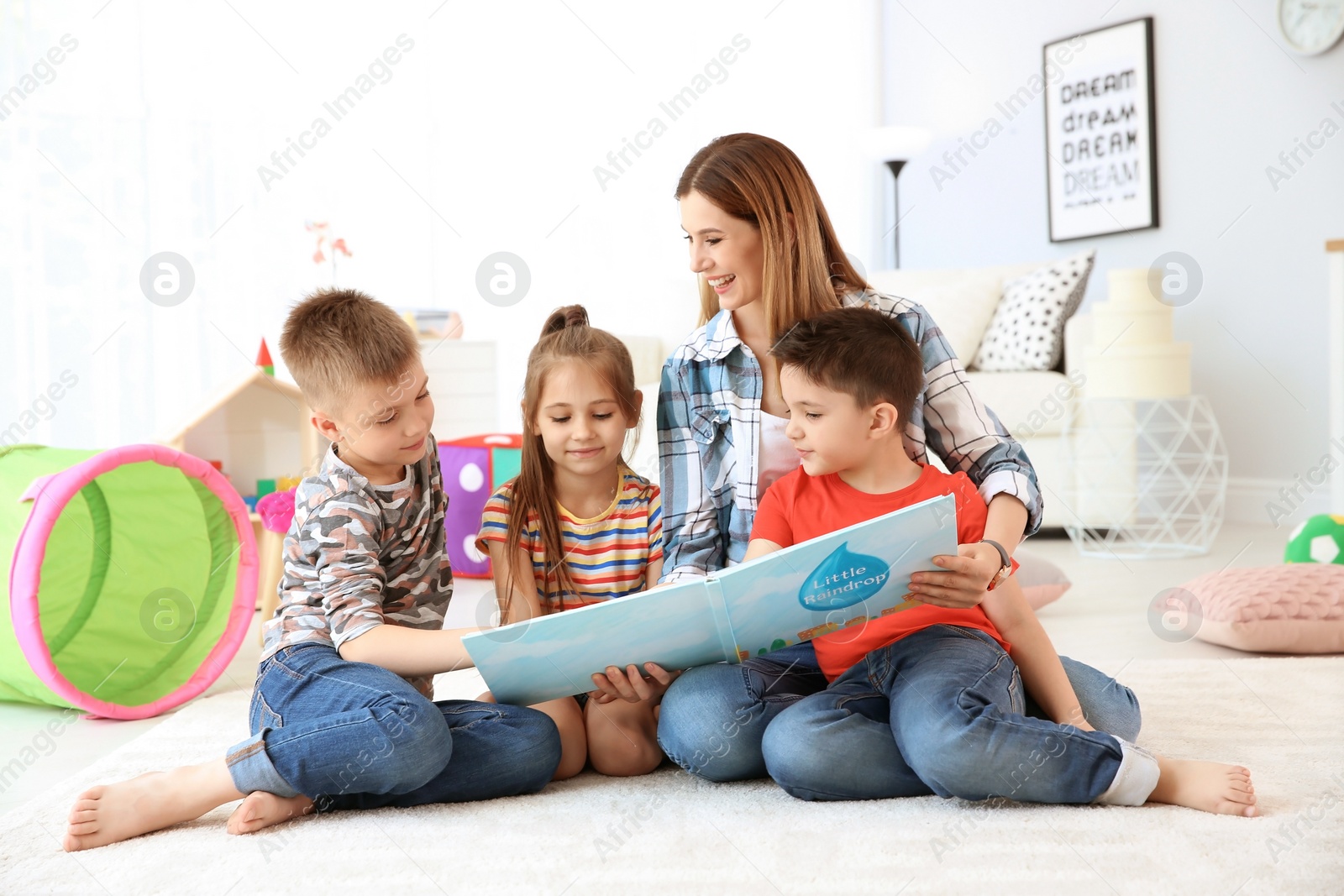 Photo of Cute little children reading book on floor with young mother in playing room