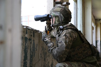 Military mission. Soldier in uniform with binoculars inside abandoned building