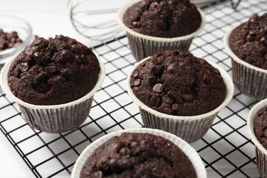 Tasty chocolate muffins and cooling rack on white table, closeup