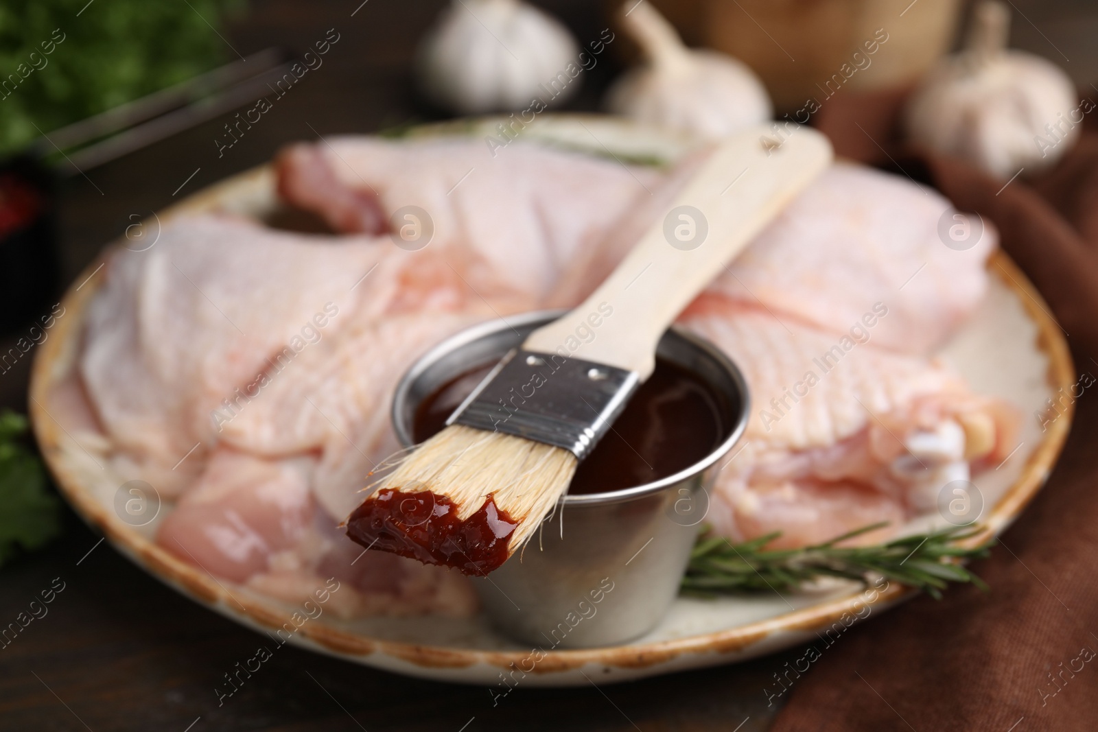 Photo of Plate with marinade, raw chicken and basting brush on table, closeup