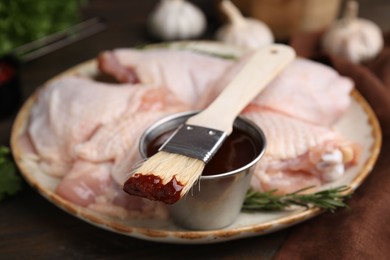 Photo of Plate with marinade, raw chicken and basting brush on table, closeup