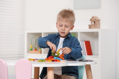 Photo of Cute little boy playing with colorful wooden pieces at white table indoors. Child's toy