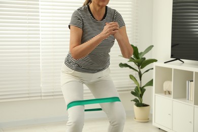 Photo of Senior woman doing squats with fitness elastic band at home, closeup