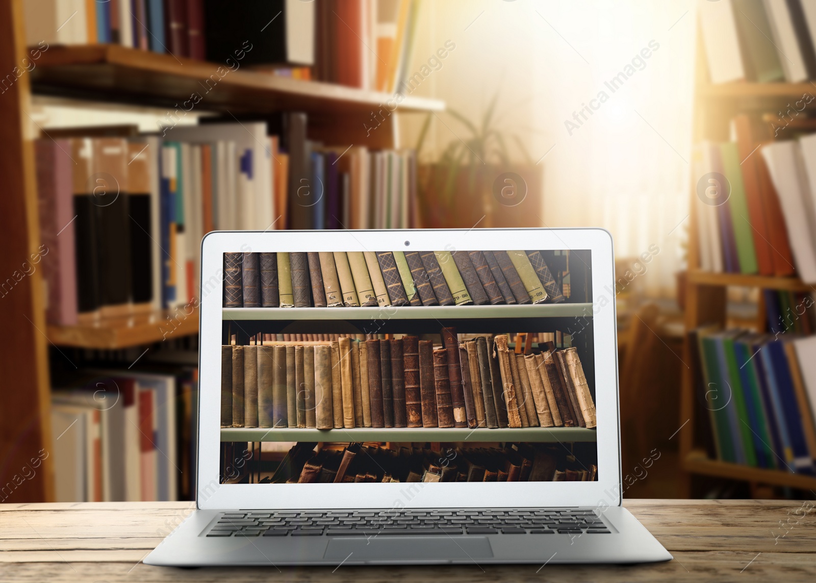 Image of Online library. Modern laptop on wooden table and shelves with books indoors