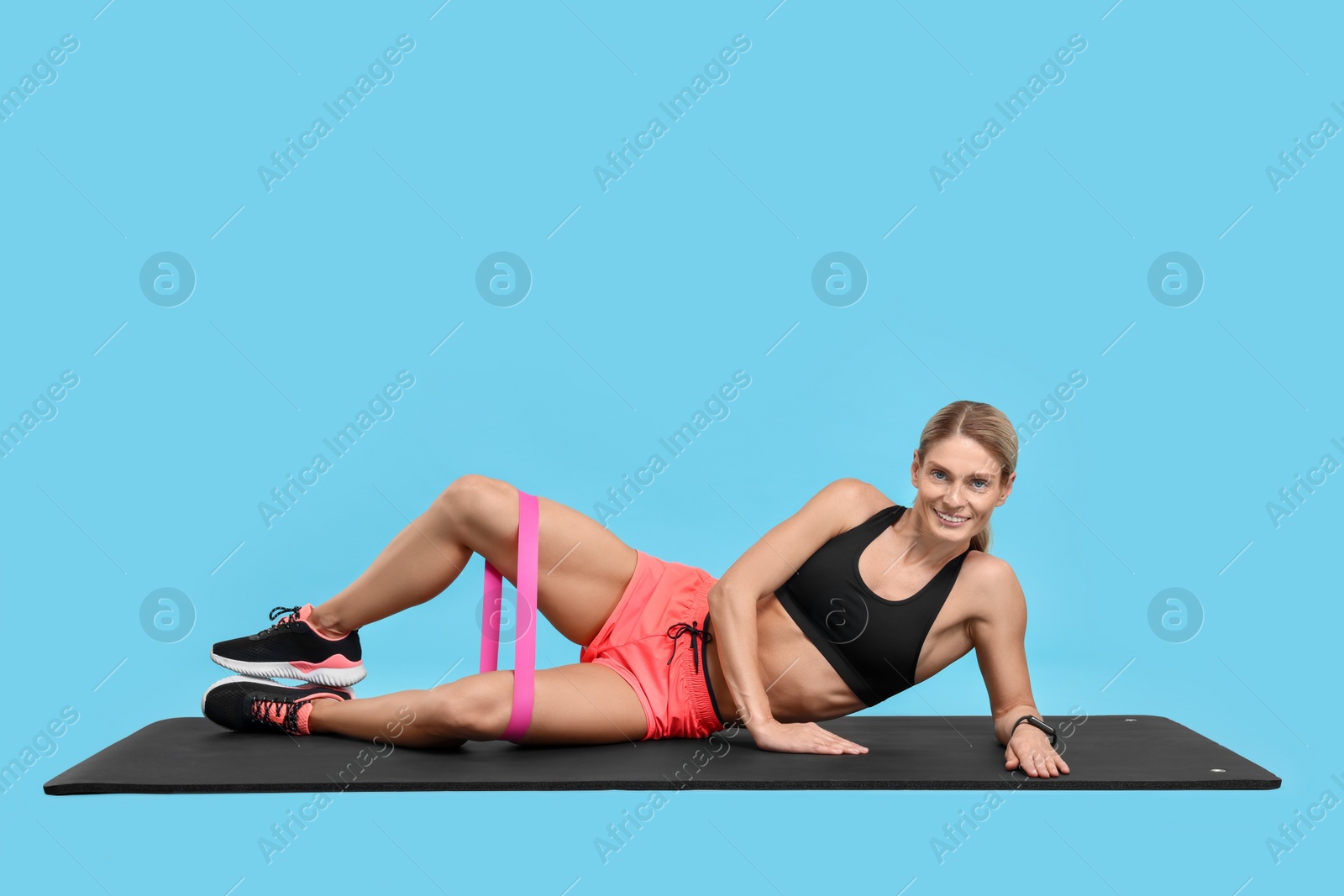 Photo of Woman exercising with elastic resistance band on fitness mat against light blue background