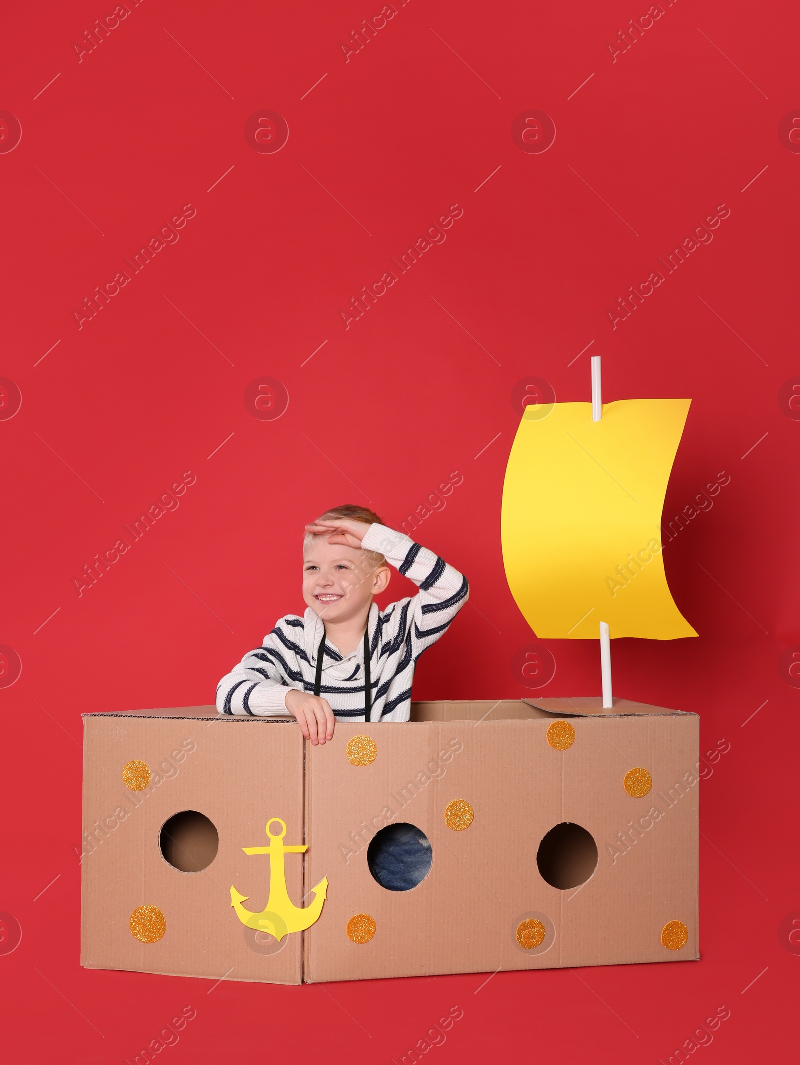 Photo of Little child playing with ship made of cardboard box on red background