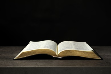Photo of Open Bible on grey table against black background