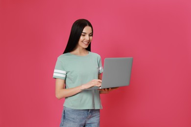 Young woman with modern laptop on pink background
