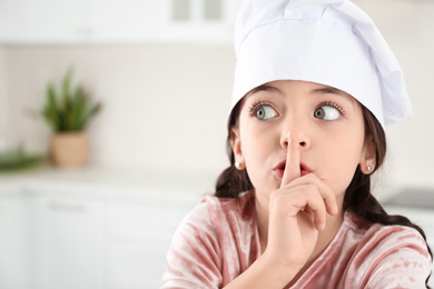 Photo of Cute little girl wearing chef hat in kitchen