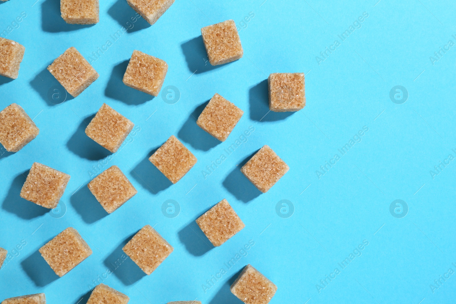 Photo of Brown sugar cubes on light blue background, top view. Space for text