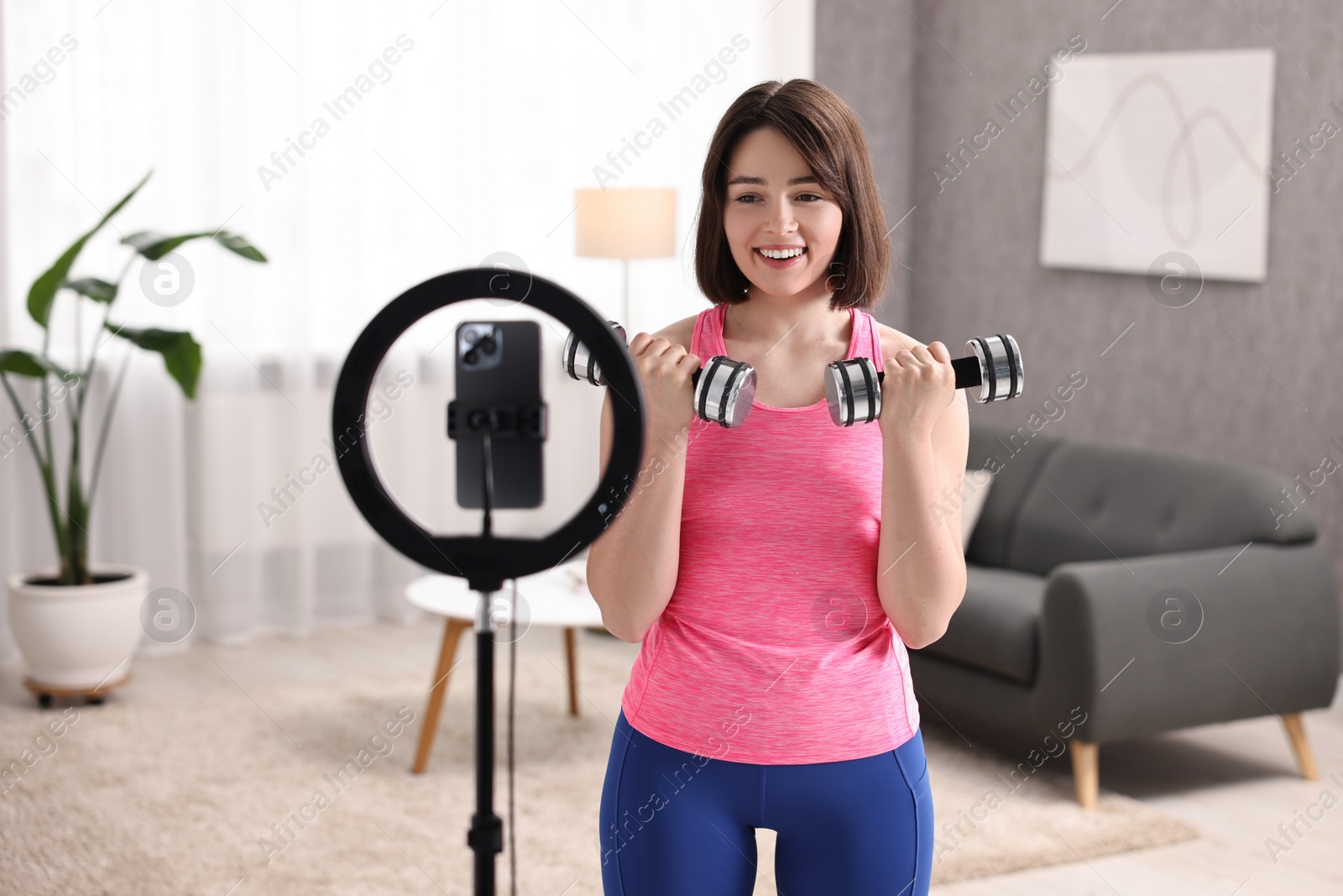 Photo of Happy sports blogger with dumbbells streaming online fitness lesson with smartphone at home