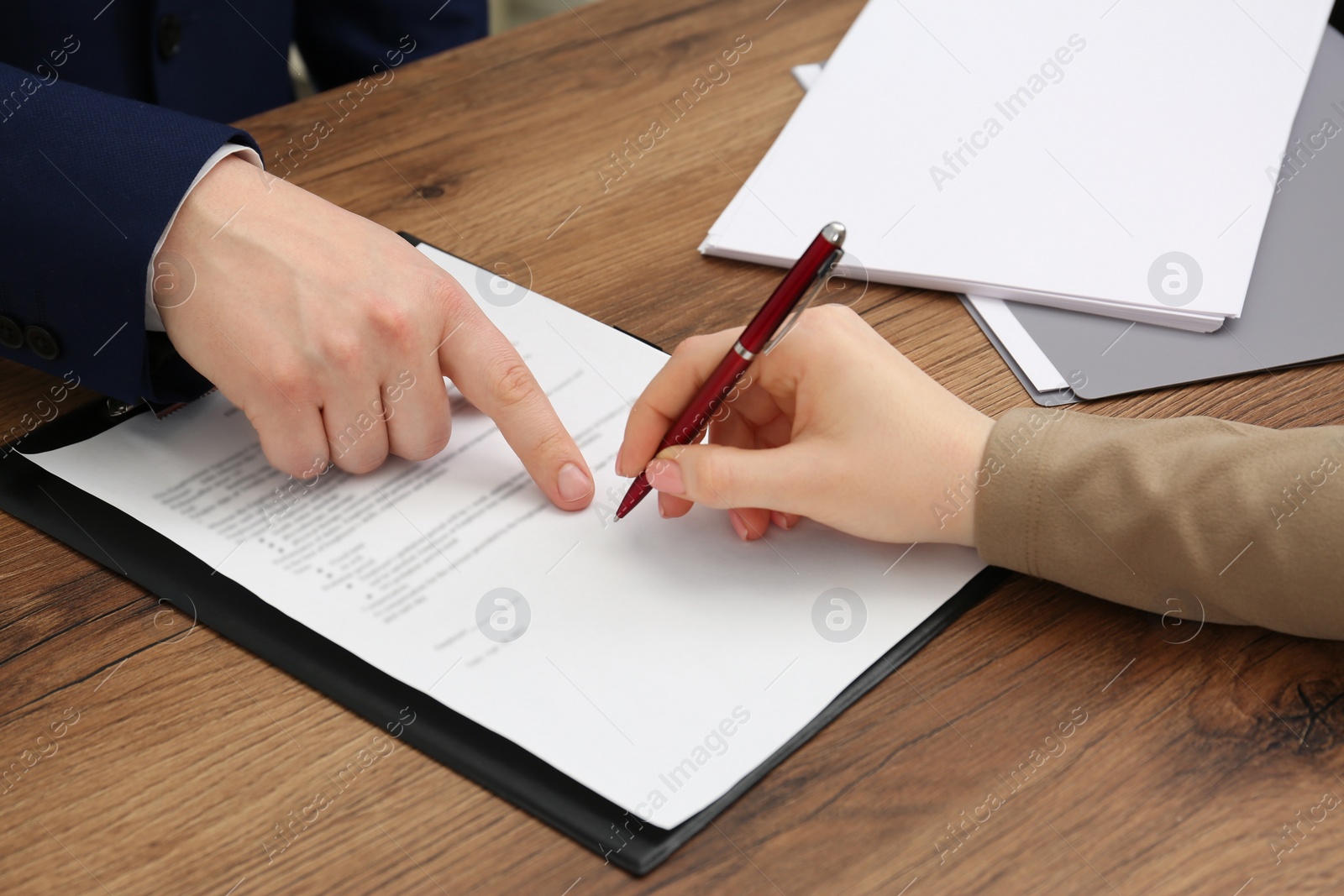 Photo of Man pointing at document and woman putting signature at wooden table, closeup