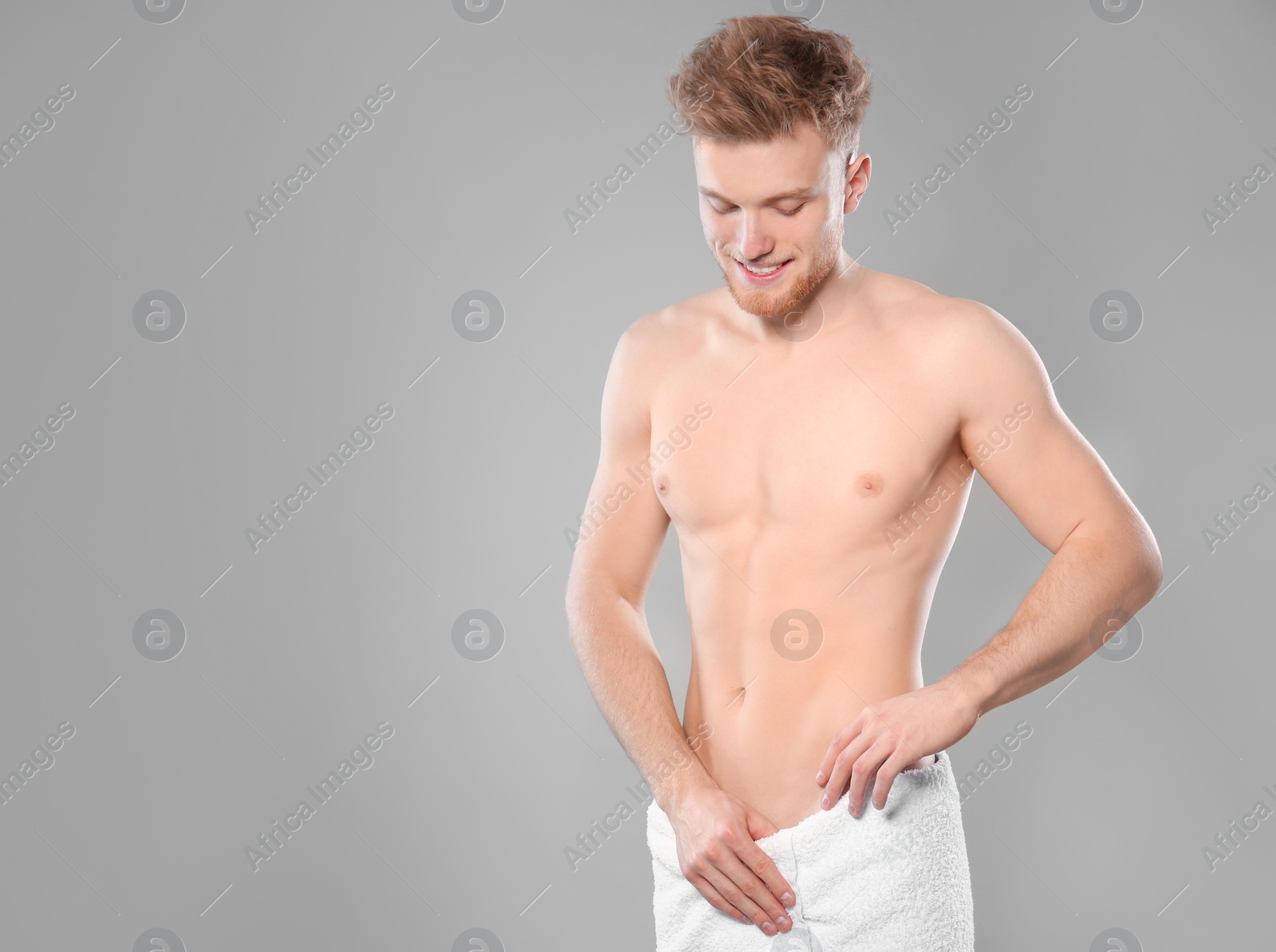 Photo of Portrait of young man with slim body in towel on grey background. Space for text