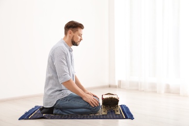 Photo of Muslim man with Koran praying on rug indoors. Space for text