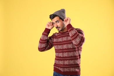 Portrait of young man in Christmas sweater and hat on yellow background