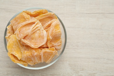 Photo of Delicious dried jackfruit slices in glass bowl on light wooden table, top view. Space for text