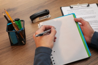 Man taking notes at wooden table, closeup