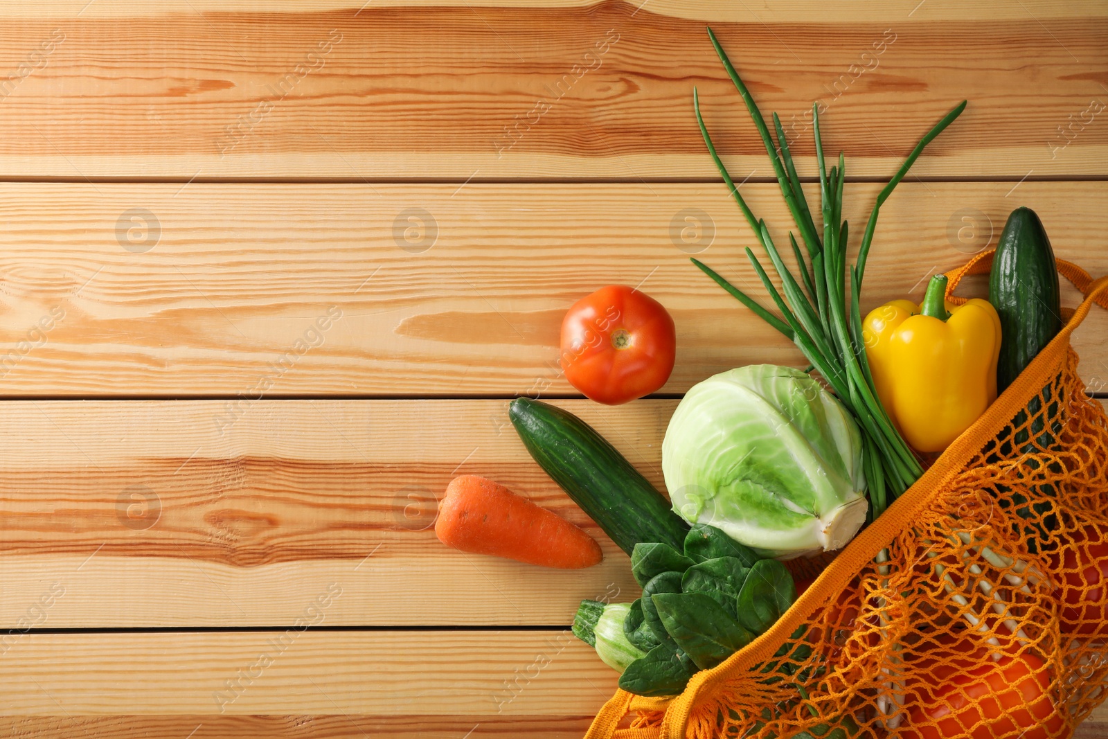 Photo of Net bag with vegetables and fruits on wooden table, flat lay. Space for text