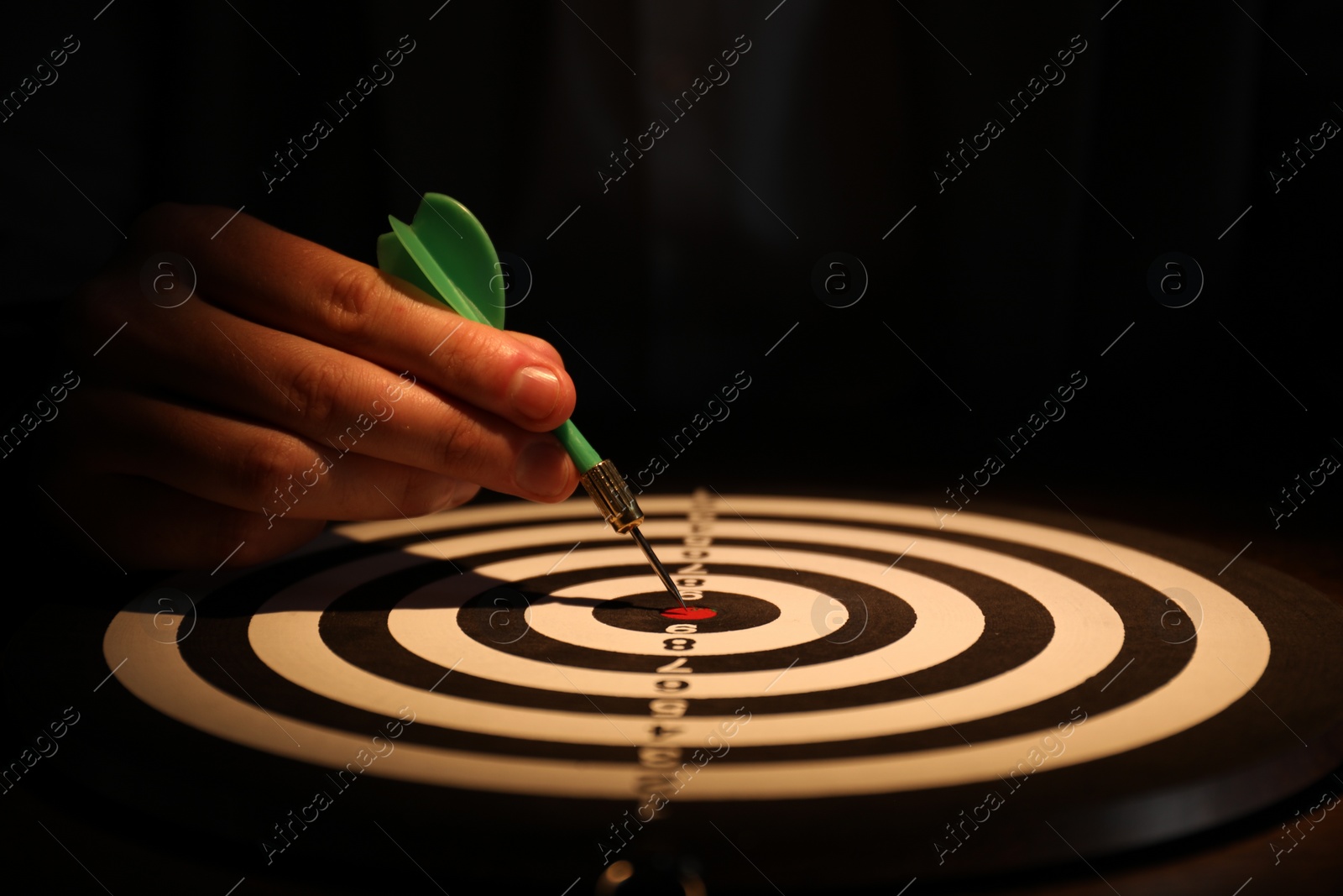 Photo of Business targeting concept. Man with dart aiming at dartboard at table in darkness, closeup