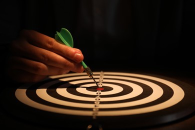 Business targeting concept. Man with dart aiming at dartboard at table in darkness, closeup