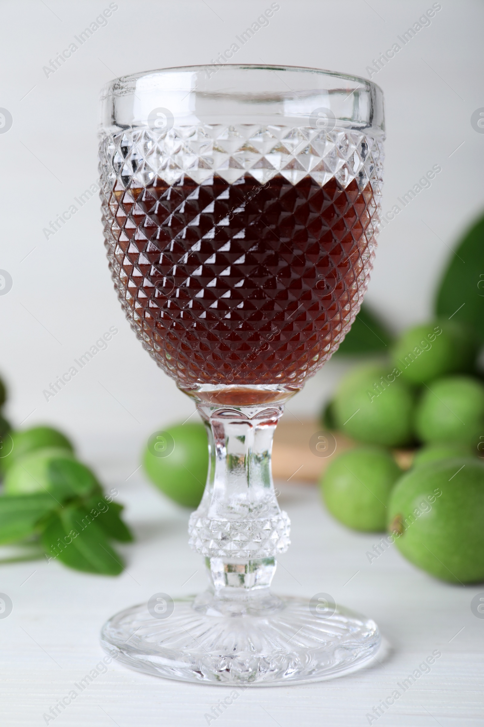 Photo of Delicious liqueur and green walnuts on white wooden table, closeup