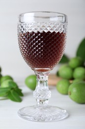 Photo of Delicious liqueur and green walnuts on white wooden table, closeup