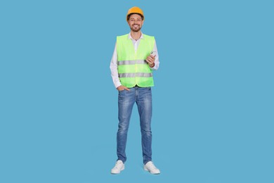 Male industrial engineer in uniform with phone on light blue background