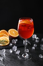 Glass of tasty Aperol spritz cocktail with orange slices and ice cubes on table against black background