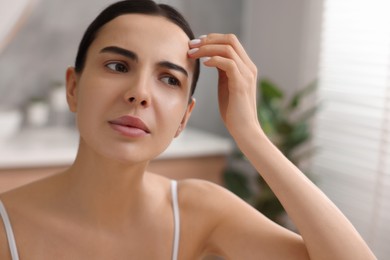 Woman with dry skin looking at mirror indoors