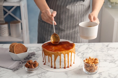 Young woman applying caramel sauce onto delicious homemade cake at table