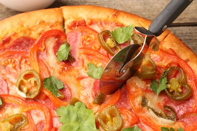 Photo of Cutting delicious pizza Diablo at table, closeup