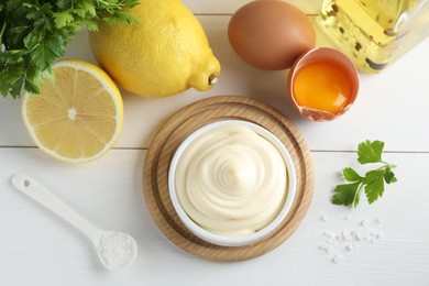 Photo of Fresh mayonnaise sauce in bowl and ingredients on white wooden table, flat lay