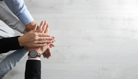 Photo of People holding hands together over light wooden background, top view with space for text. Unity concept