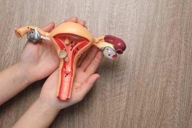 Photo of Woman with anatomical model of uterus at wooden table, top view and space for text. Gynecology concept
