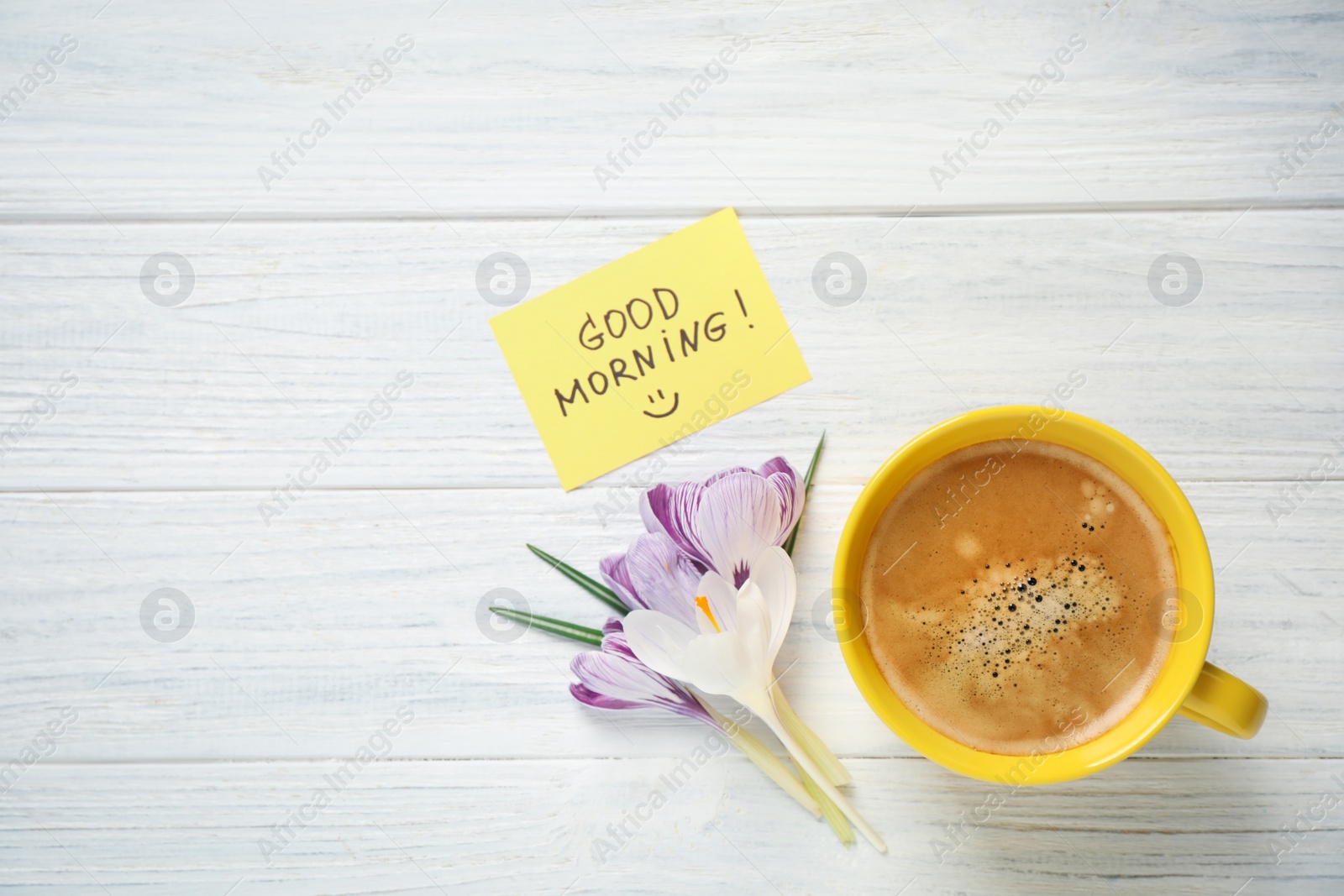 Photo of Delicious coffee, flowers and card with GOOD MORNING wish on white wooden table, flat lay. Space for text