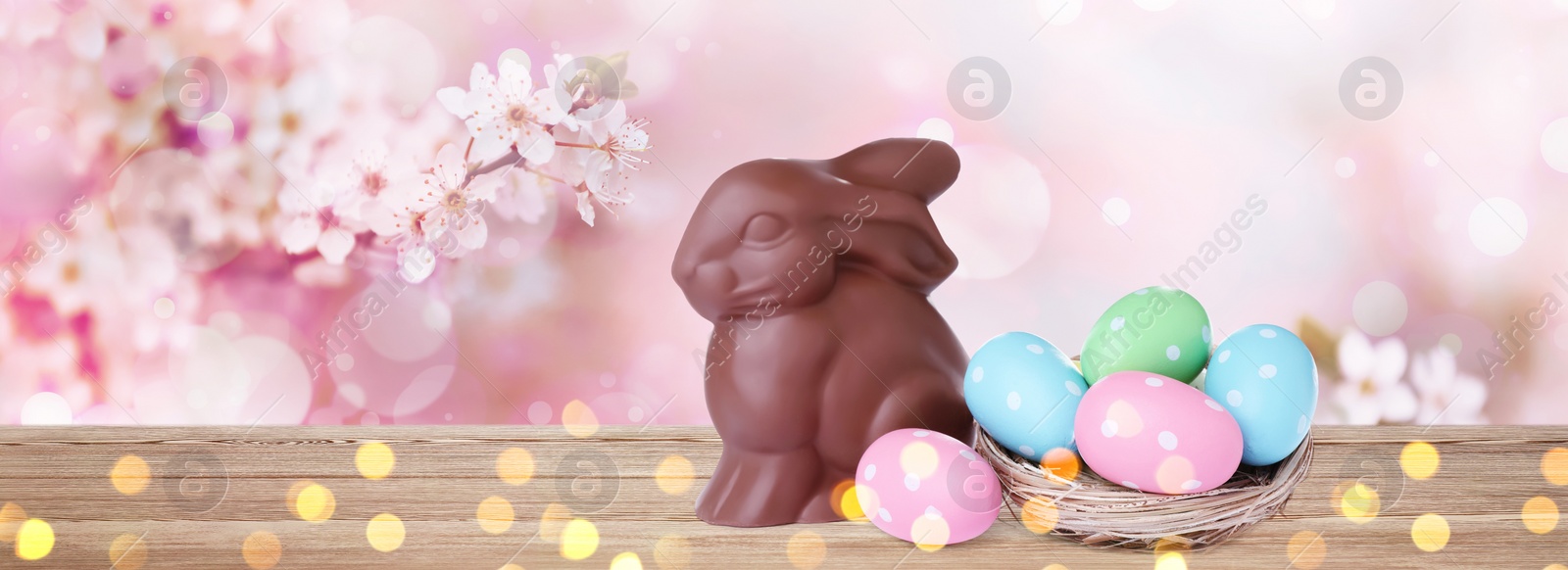 Image of Sweet chocolate bunny and colorful eggs on wooden table outdoors, banner design. Easter celebration