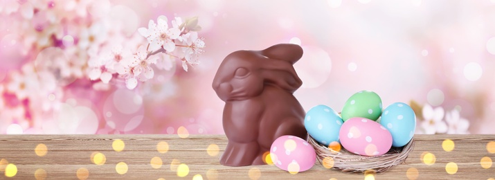 Sweet chocolate bunny and colorful eggs on wooden table outdoors, banner design. Easter celebration