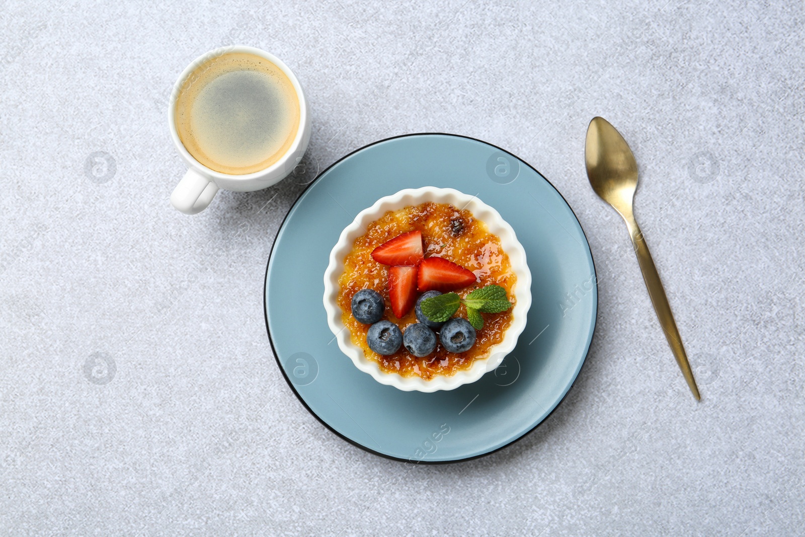 Photo of Delicious creme brulee with berries and mint in bowl served on grey textured table, flat lay