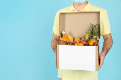 Photo of Courier holding box with assortment of exotic fruits on turquoise background, closeup. Space for text