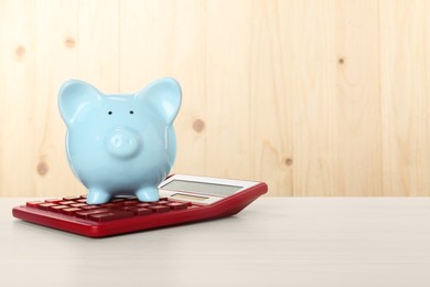 Photo of Calculator and piggy bank on light wooden table. Space for text